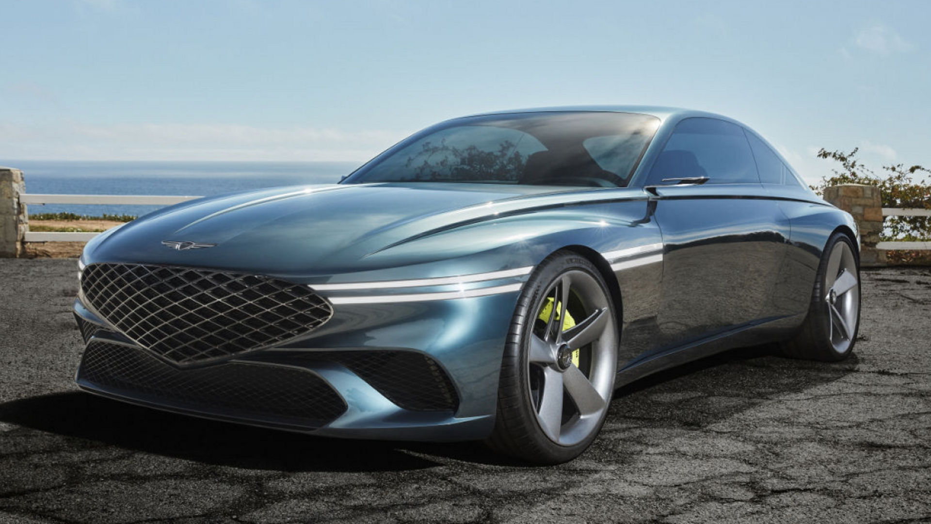 Genesis X Concept stands in a car park by the sea - front side view