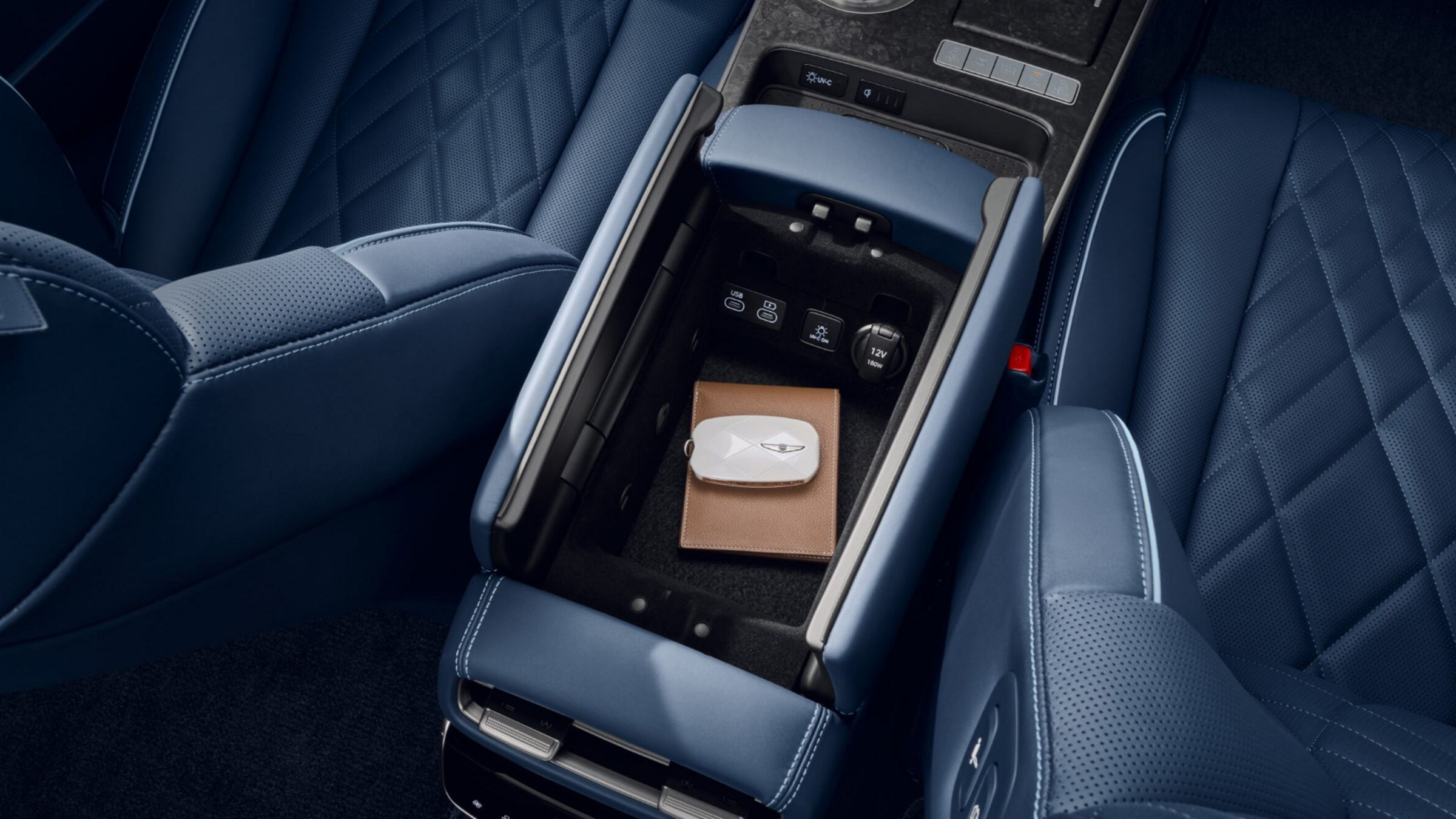 UV-C ON button, and a 12V/180W power socket in a storage bin in the front seat console armrest. The bin contains a smart key with the white Genesis logo and a light brown wallet.