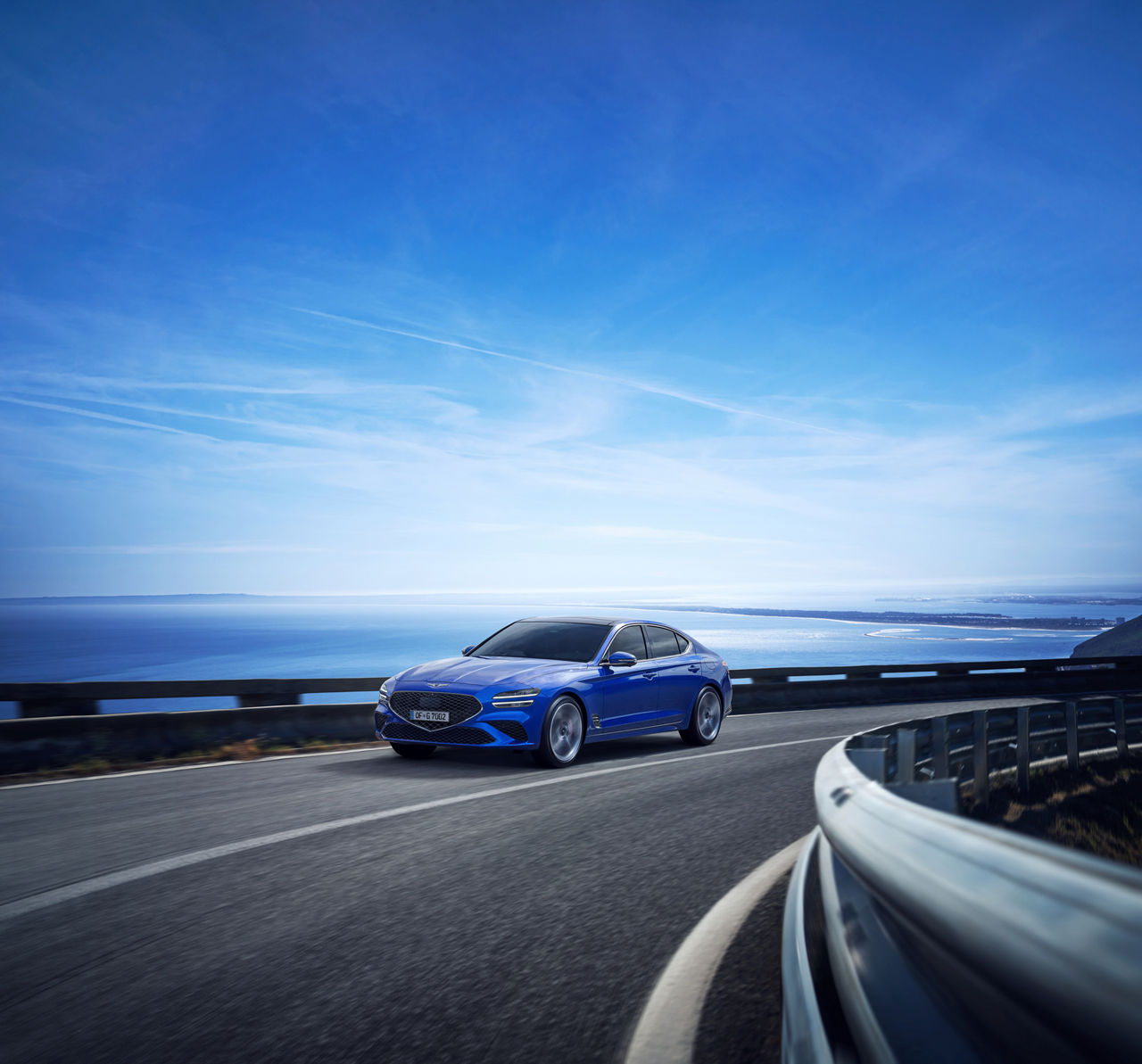 Blue Genesis G70 on a road with the sea in the background
