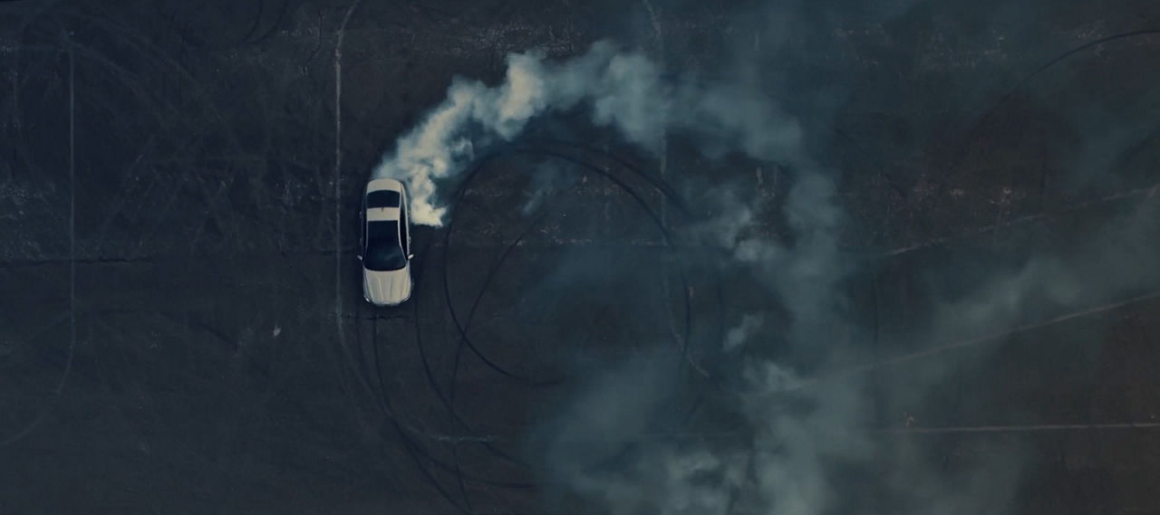 Aerial view of a white car driving in circles and trailing a trail of smoke behind it