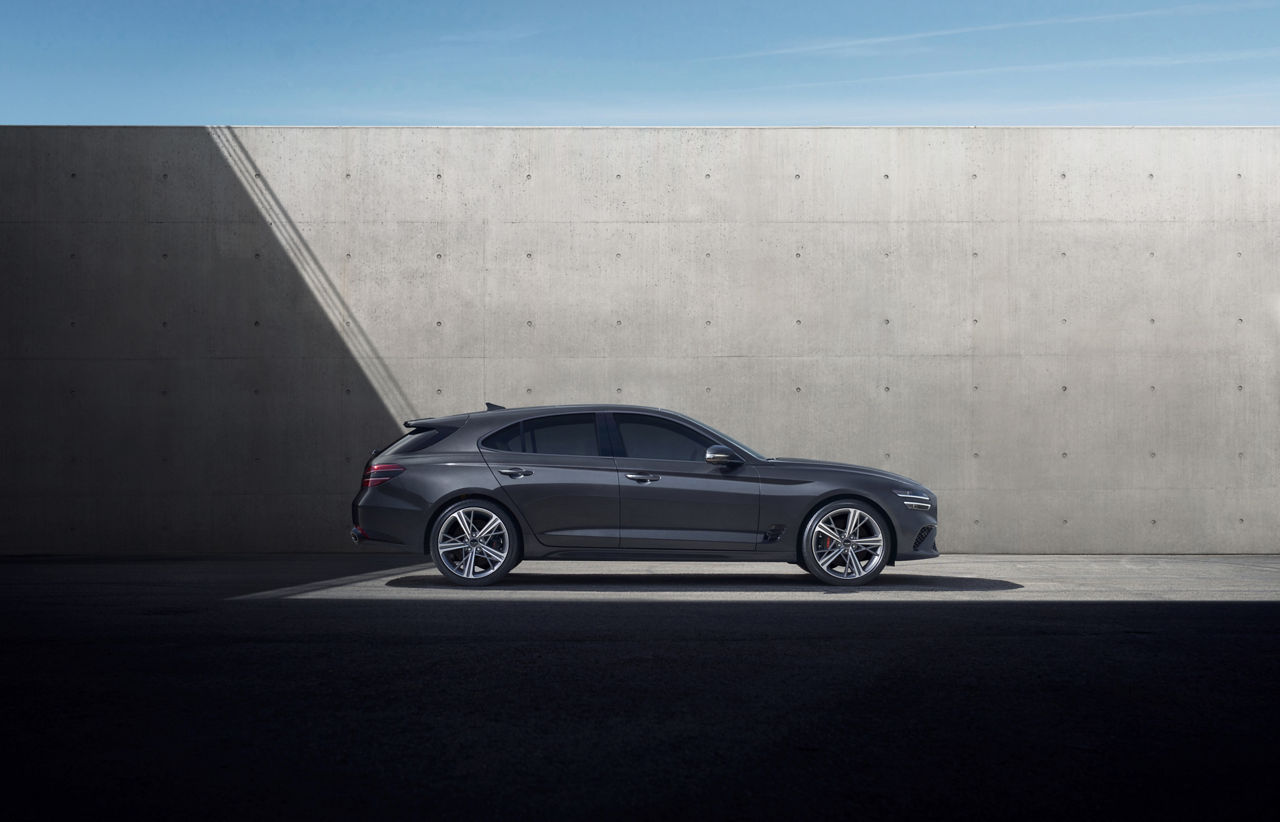 A grey Genesis G70 from the side in front of a wall