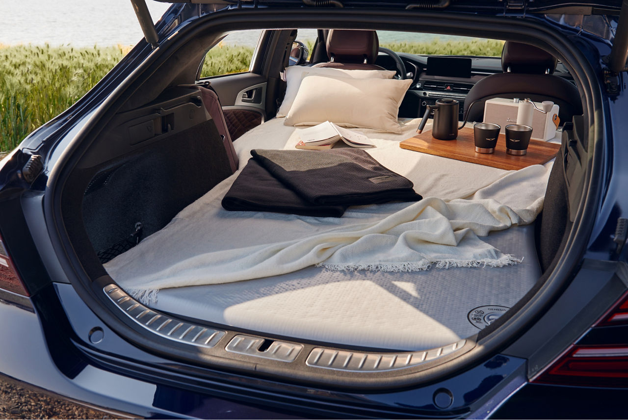 Kofferraum und umgeklappte Rücksitze eines Autos mit einer Matratze, Kissen und Decken darin