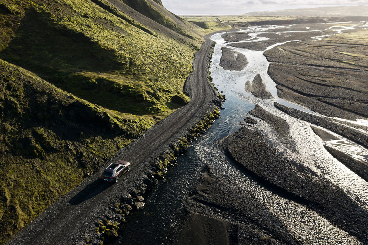 Aerial shot of a car on a road between a mountain and a river