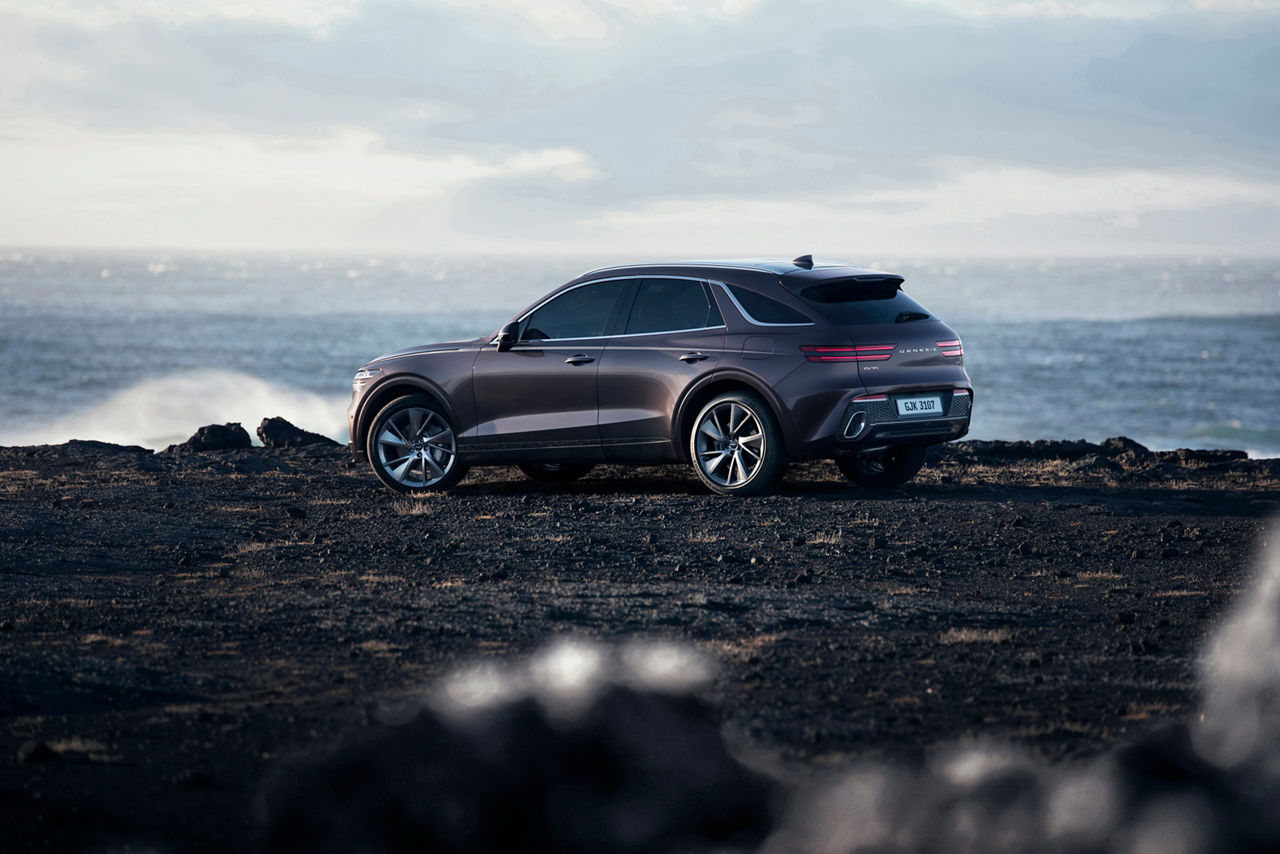 Side view of the Genesis GV70 Burgundy on the coast of Iceland with the sea in the background