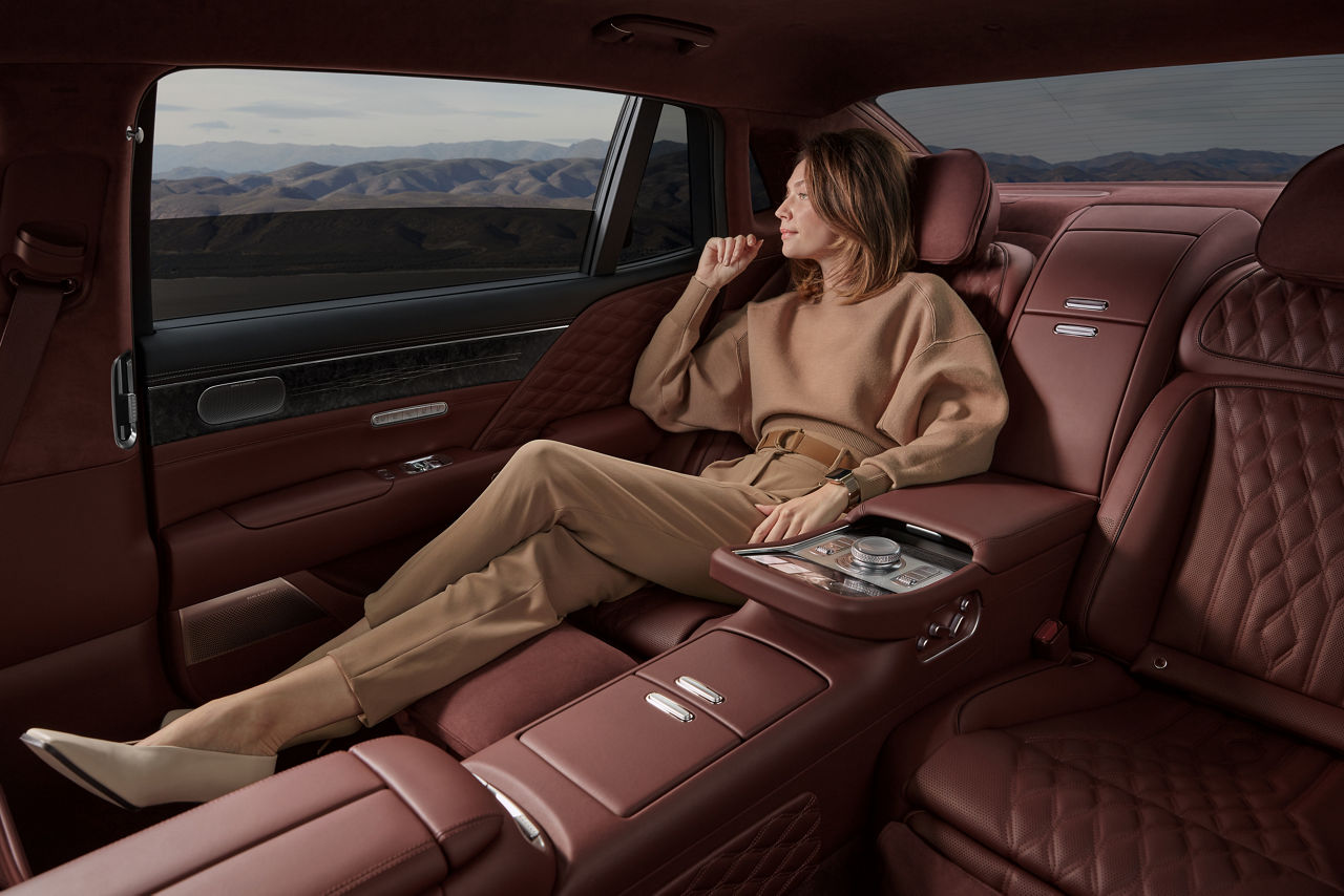Woman sits relaxed in the back seat of the Genesis G90 and looks out of the window