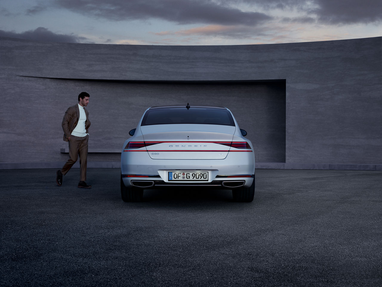 White Genesis G90 from behind with a man next to it in front of a wall