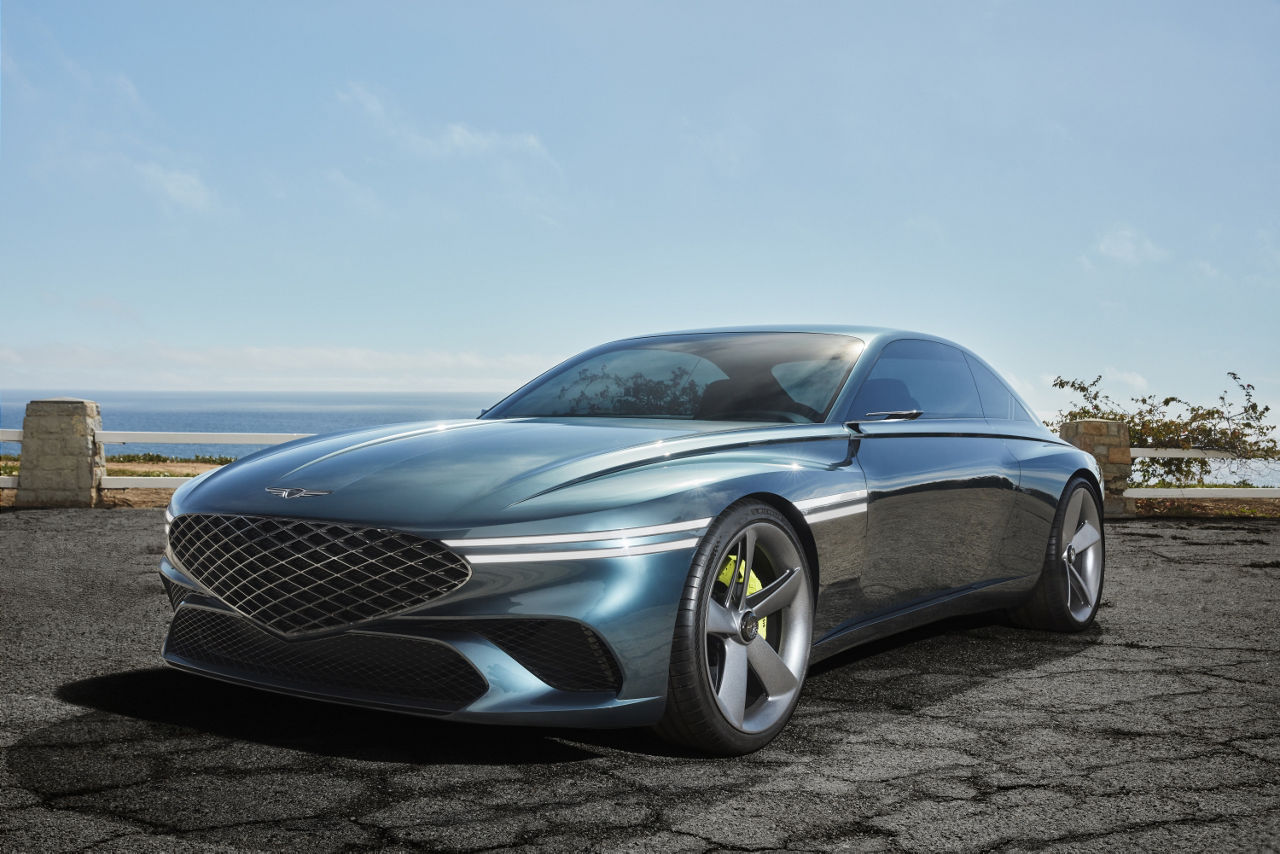 Genesis X Concept stands in a car park by the sea - front side view