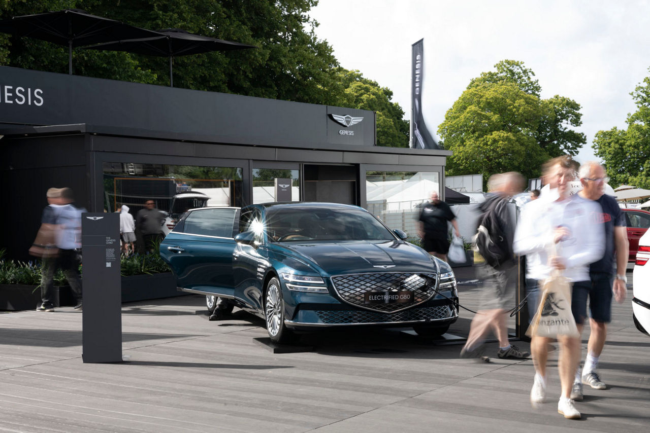 Blue Genesis G80 in front of a building at an outdoor event