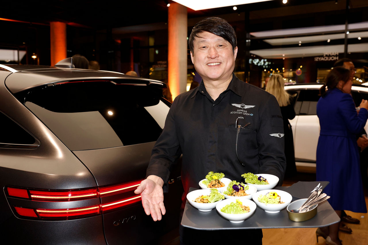 Chef presents a tray of food in the Genesis Studio next to a grey GV70