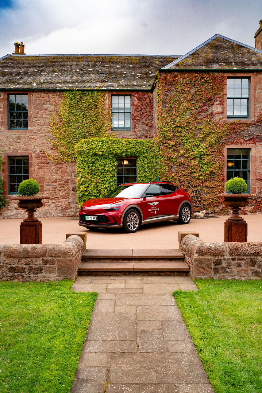 Red Genesis GV 60 in front of a house with ivy on the wall