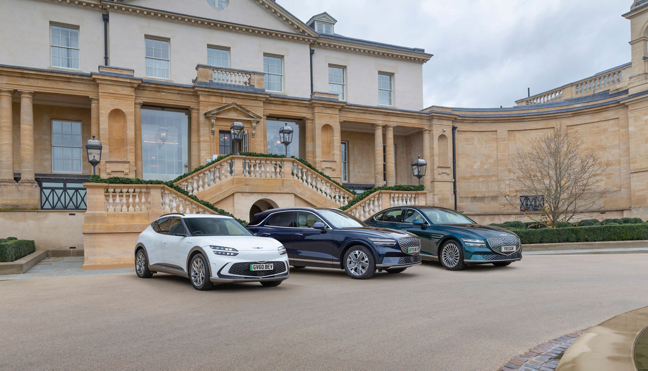 Three Genesis cars - a white GV60, a blue GV70 and a blue G80 - parked in front of a magnificent old building
