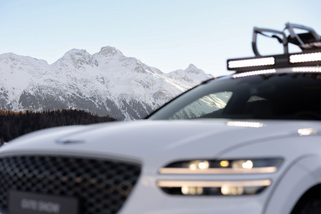 Close-up of a white Genesis GV70 with snow-covered mountains in the background