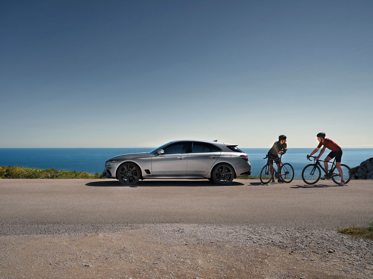 Genesis G70 Shooting Brake silver outdoor - side view in front of ocean with two cyclist