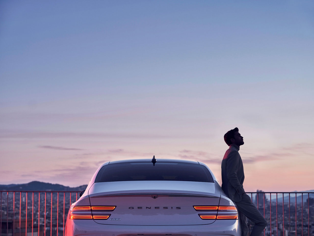 A man leans against a white Genesis Electrified G80 at sunset