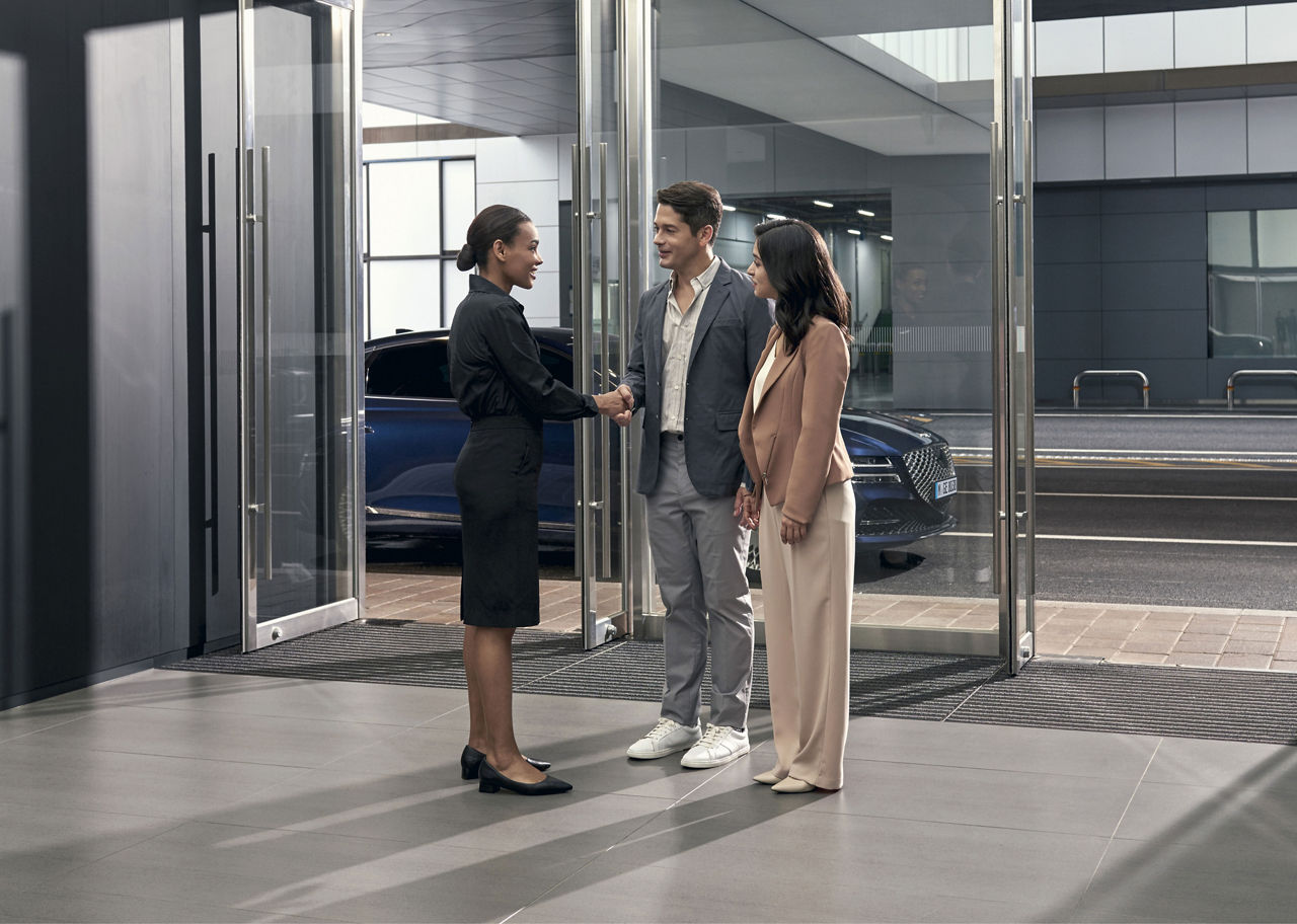 People greeted by Personal Assistant in a Genesis Studio with a blue G80 outside
