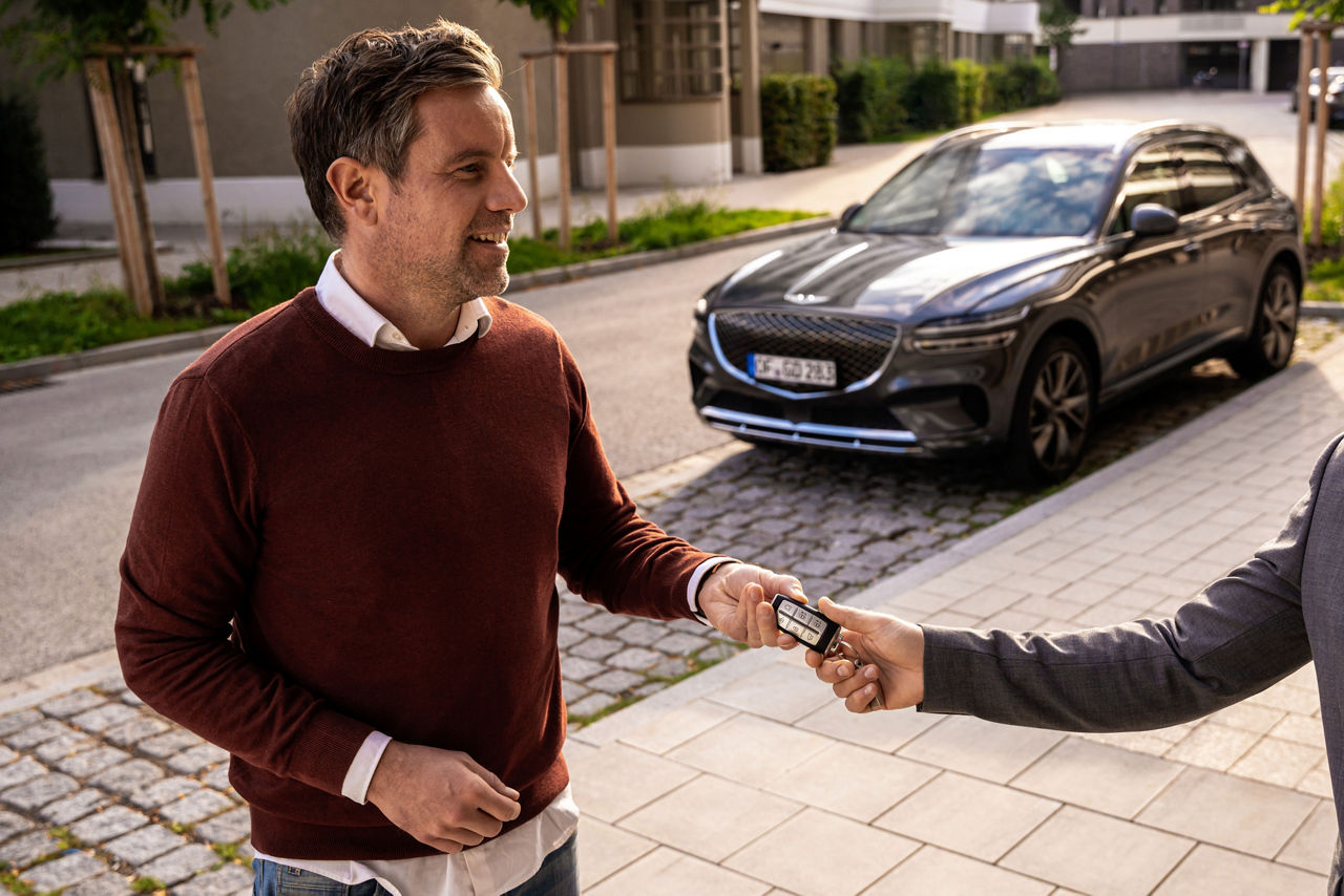 A man is given the key to a Genesis parked in the background