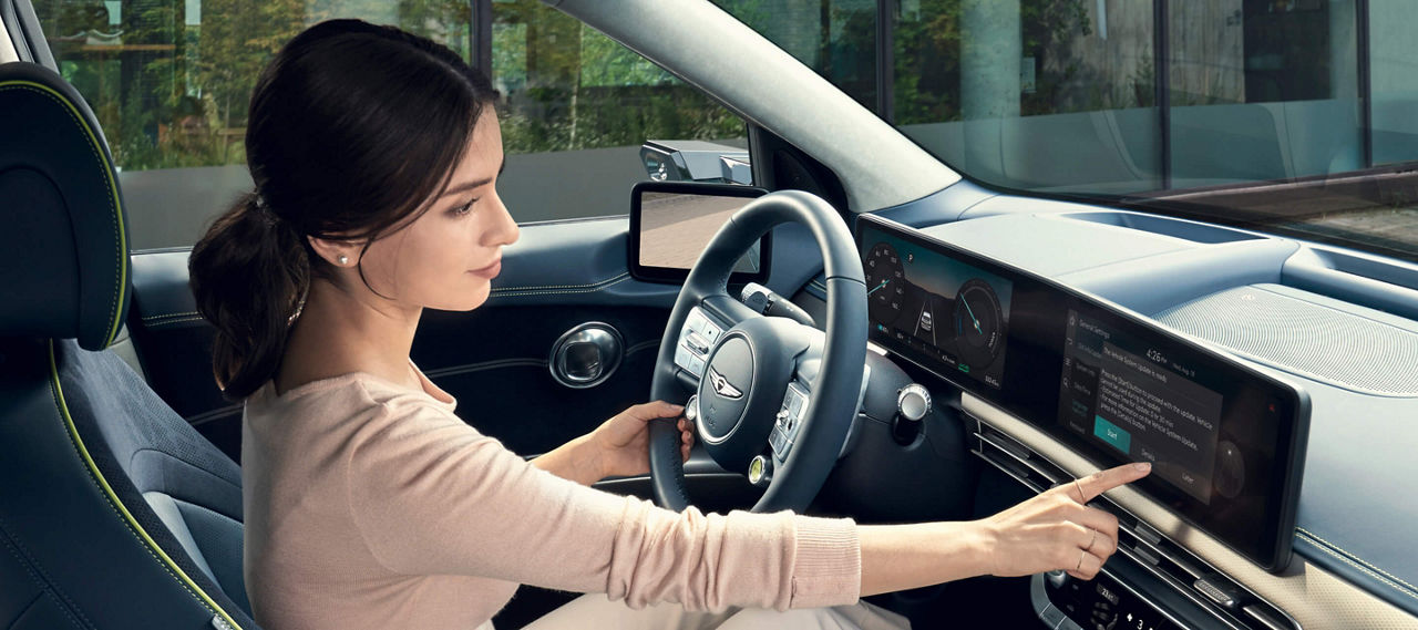 Woman in the driver's seat of the Genesis GV60, operating the display above the centre console