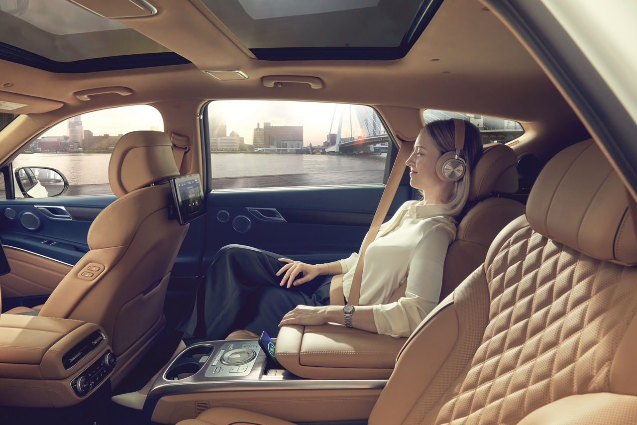 Frau sitzt entspannt mit Kopfhörern auf den Ohren auf dem Rücksitz eines Autos