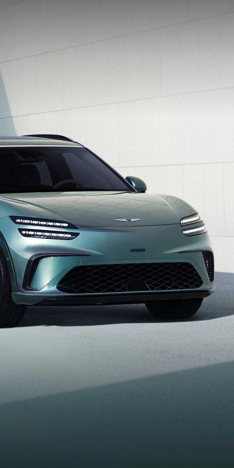 Sur fond d'un bâtiment bleu moderne, un Genesis GV60 de couleur vert Tromso est arrêtée vers la gauche.