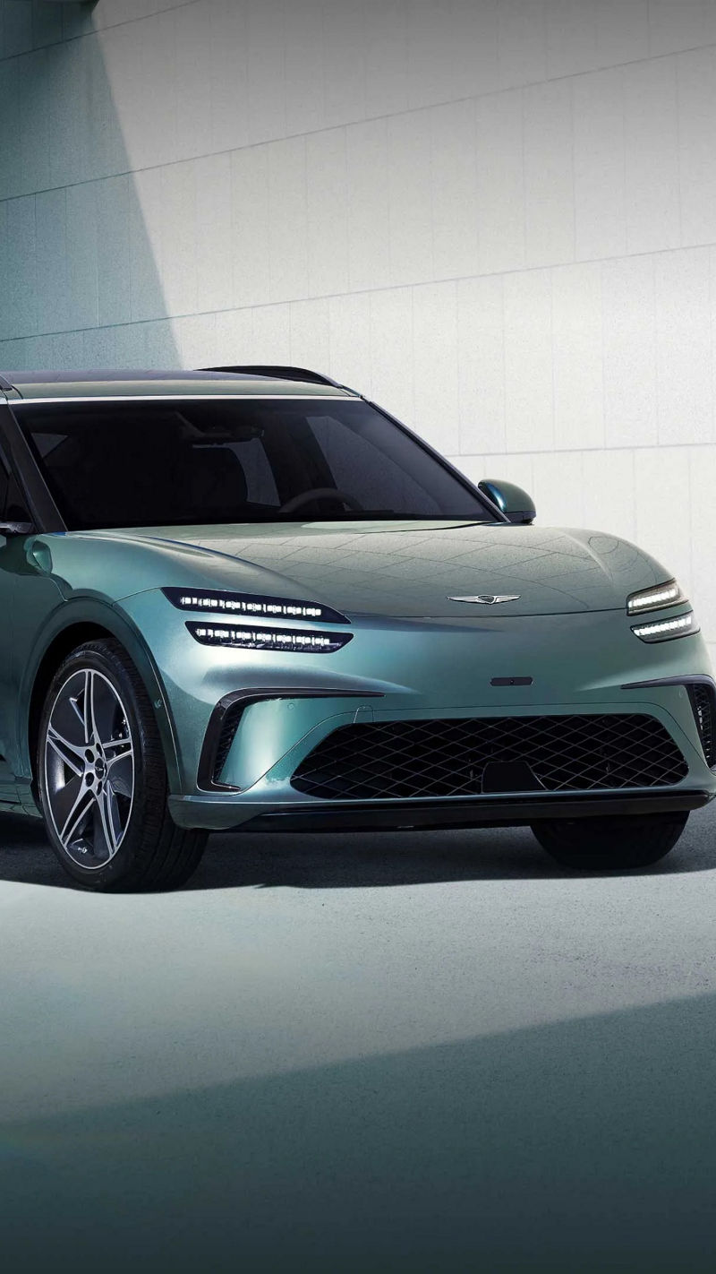  In the background of a modern blue building, a Tromso green-colored GV60 is stopped toward the left.