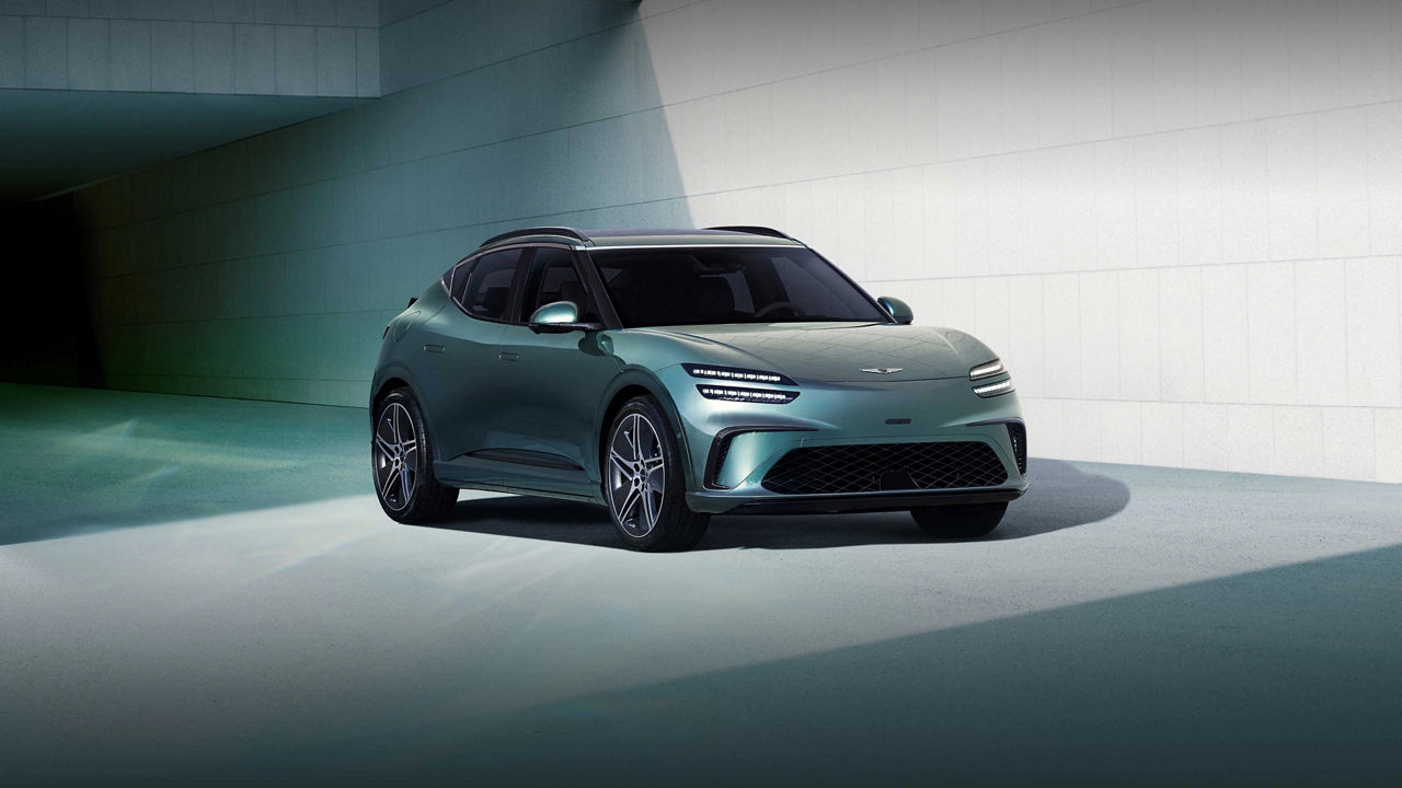  In the background of a modern blue building, a Tromso green-colored GV60 is stopped toward the left.