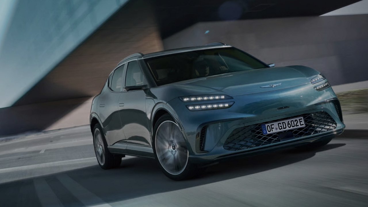 Con un edificio moderno sullo sfondo, si vede la parte anteriore del veicolo GV60 che sfreccia lungo l'autostrada.