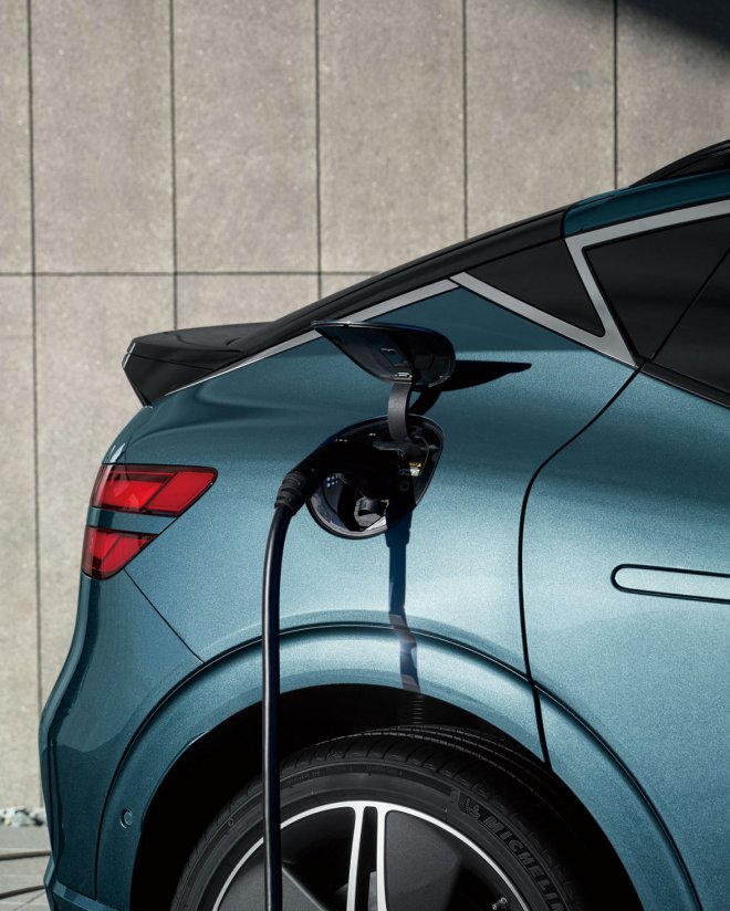 Un vehículo eléctrico Genesis EV se está cargando con un cargador doméstico Genesis instalado en la pared del edificio.