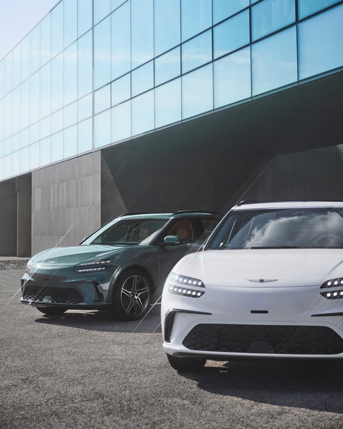 With the modern building in the background, there is a GV60 in Tromso green on the left and a GV60 in Uyuni white on the right.