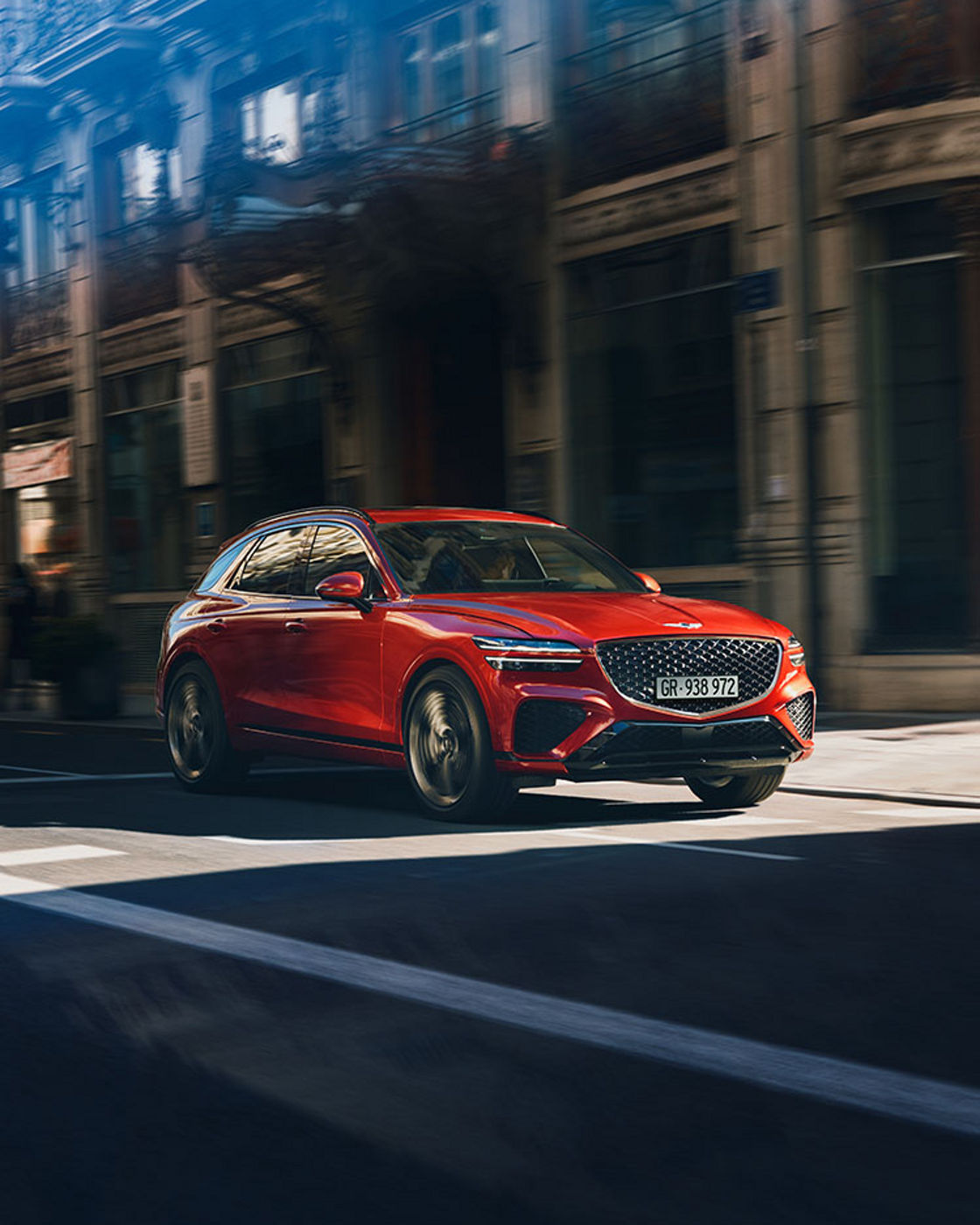 A red GV70 driving through the streets under the sunlight