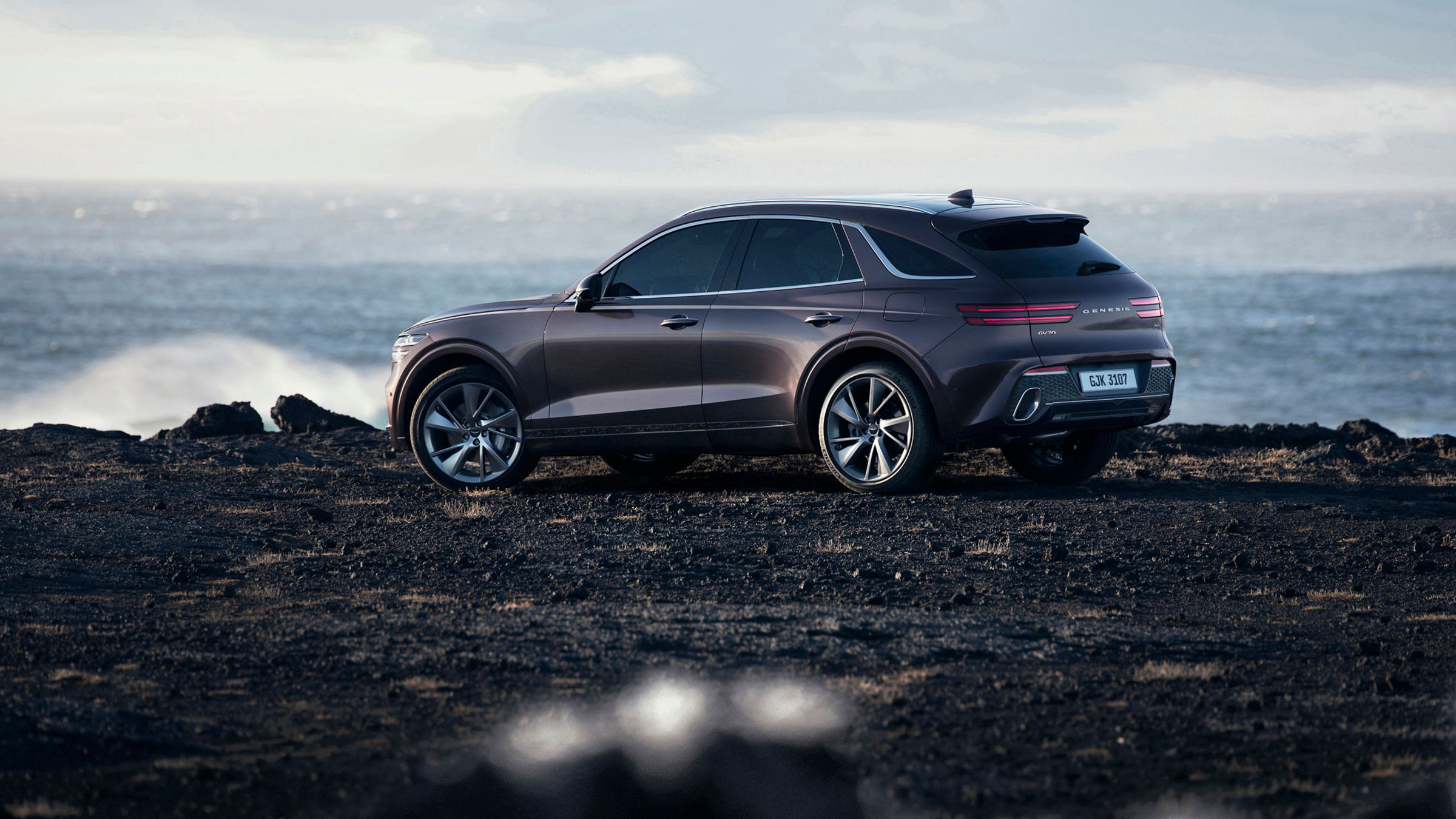 Genesis GV70 parked on a rugged coastal terrain with the ocean in the background, highlighting its elegance and adventurous spirit.