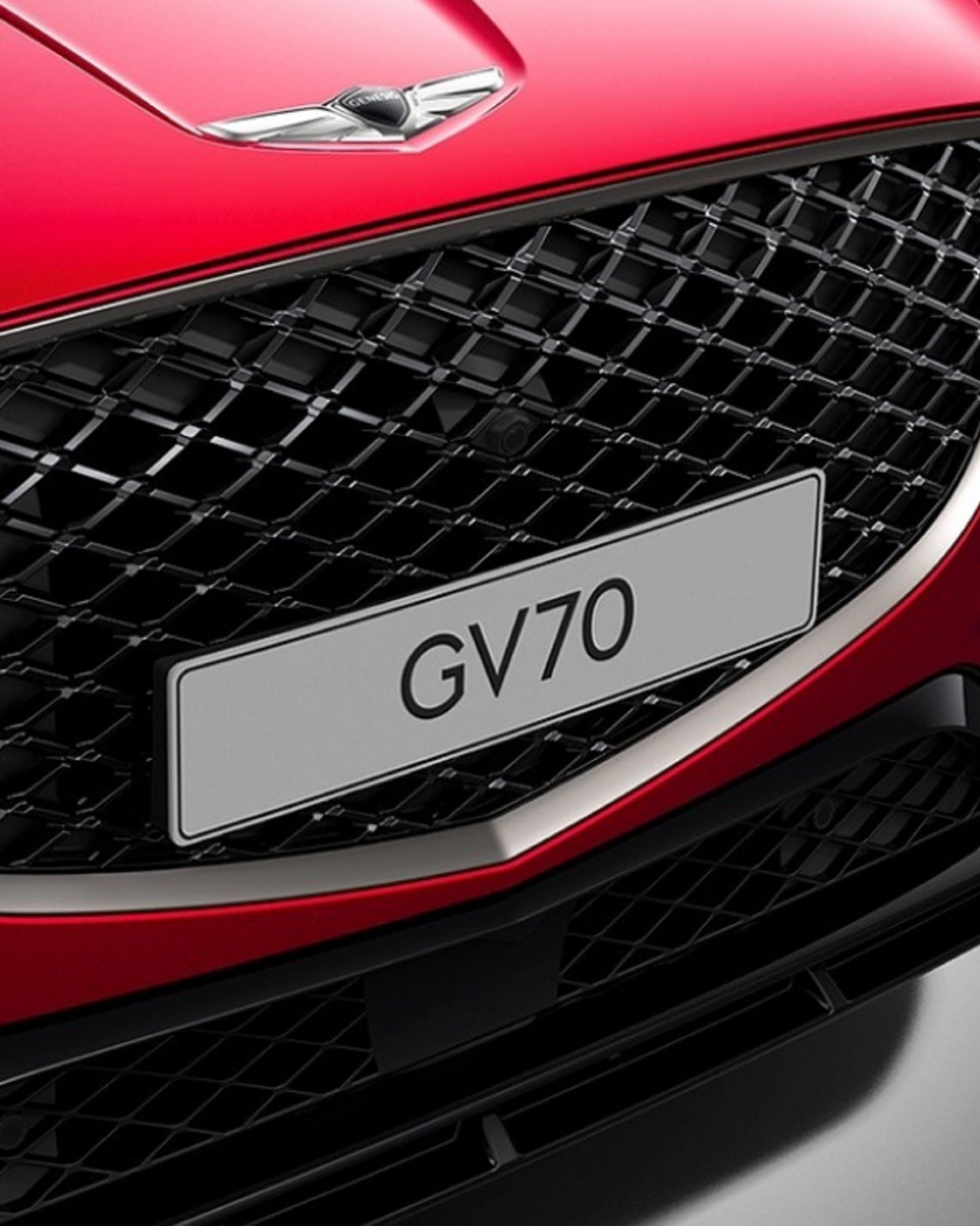 Front close-up of a red GV70 grille with a bold Genesis badge and intricate mesh pattern.