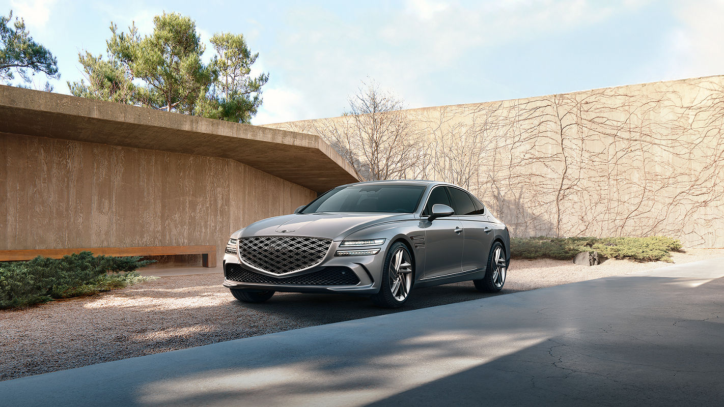 A gray Genesis G80 parked in a minimalist outdoor setting with natural elements and modern architecture.