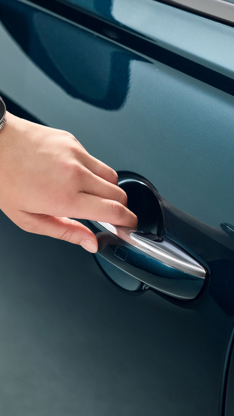 A hand wearing a smartwatch is close to a car door, attempting to remotely operate it. 