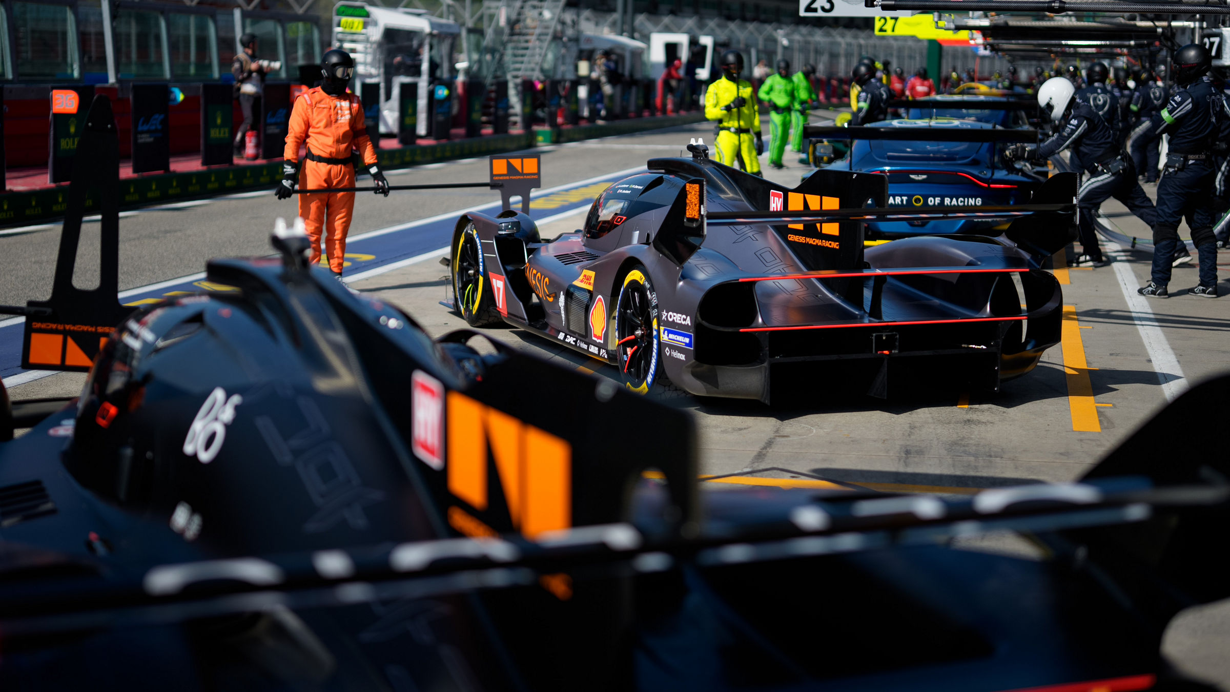 Genesis GRM-001 in pit lane during service stop with crew and marshals nearby.