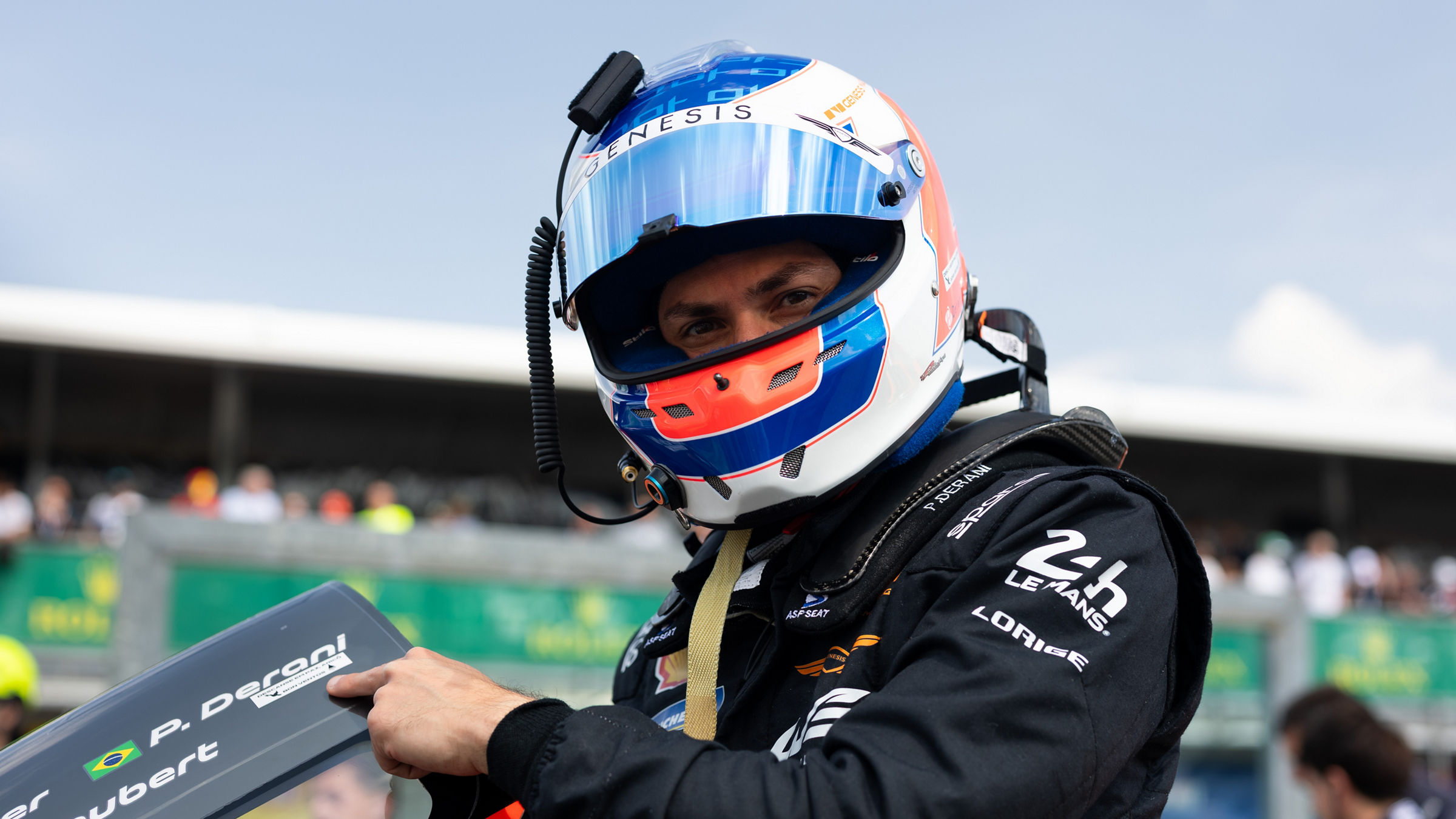 Helmeted Luis Felipe Derani holding pit board on grid.