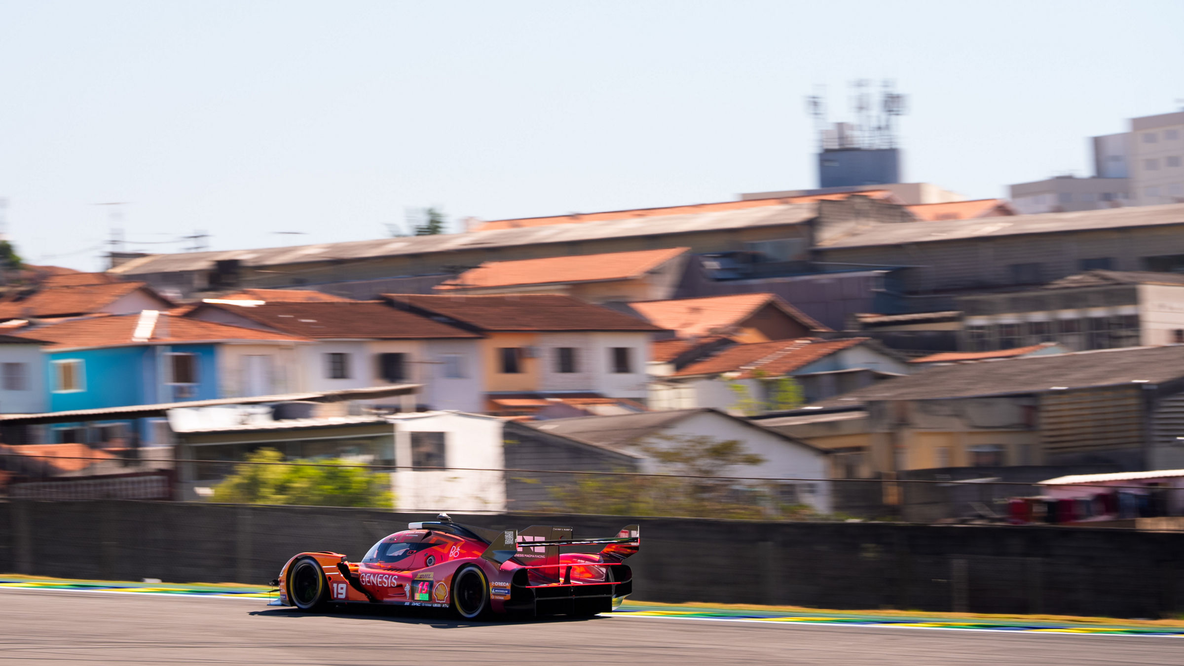 Genesis GRM-001 hypercar speeds around the Interlagos circuit during the WEC São Paulo weekend, with the city skyline and residential buildings forming the backdrop beyond the track.