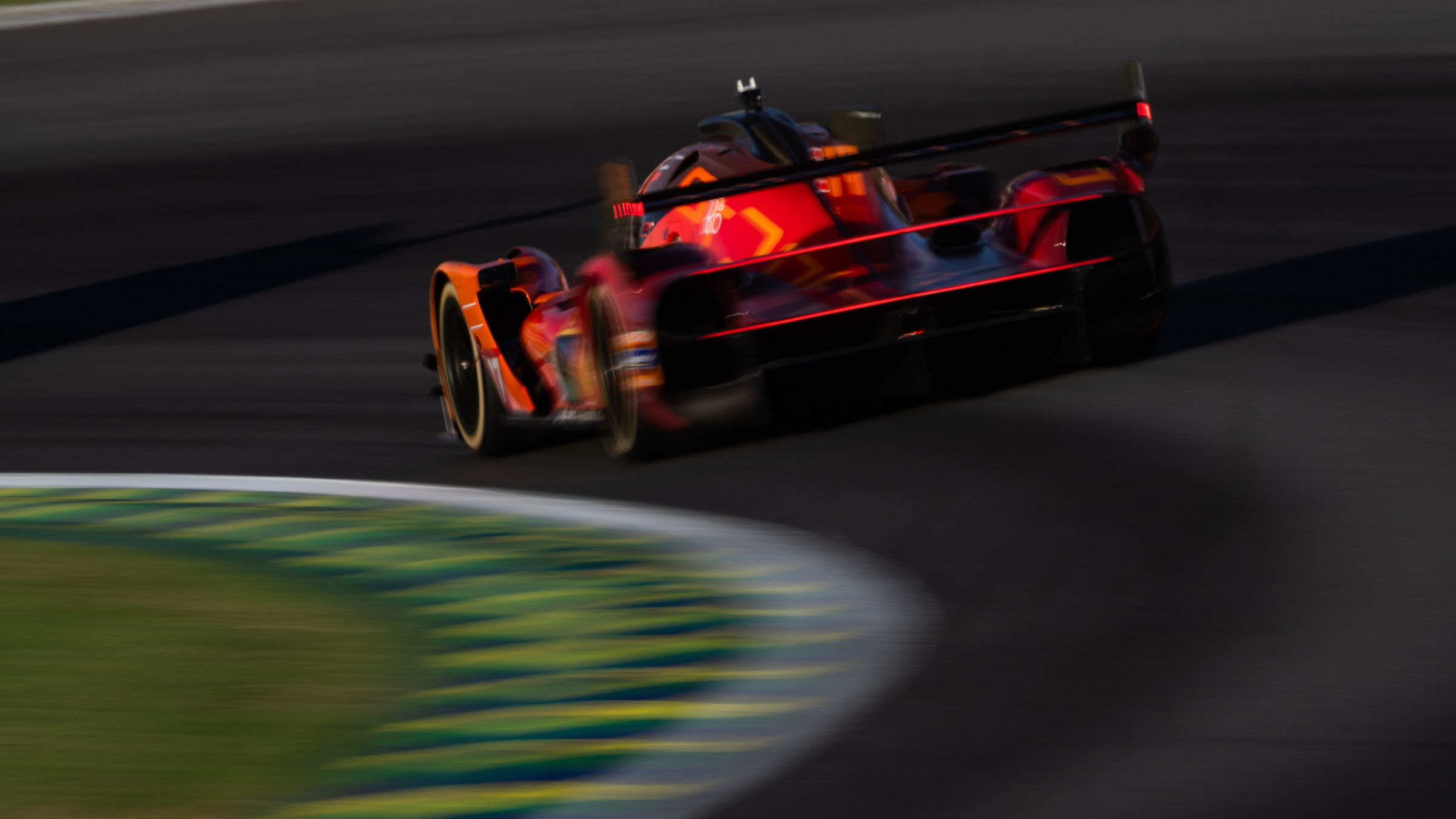 Rear view of the Genesis GRM-001 hypercar accelerating through a corner at Interlagos during the WEC São Paulo weekend, captured with motion blur that emphasizes speed and the car’s illuminated rear light strip.