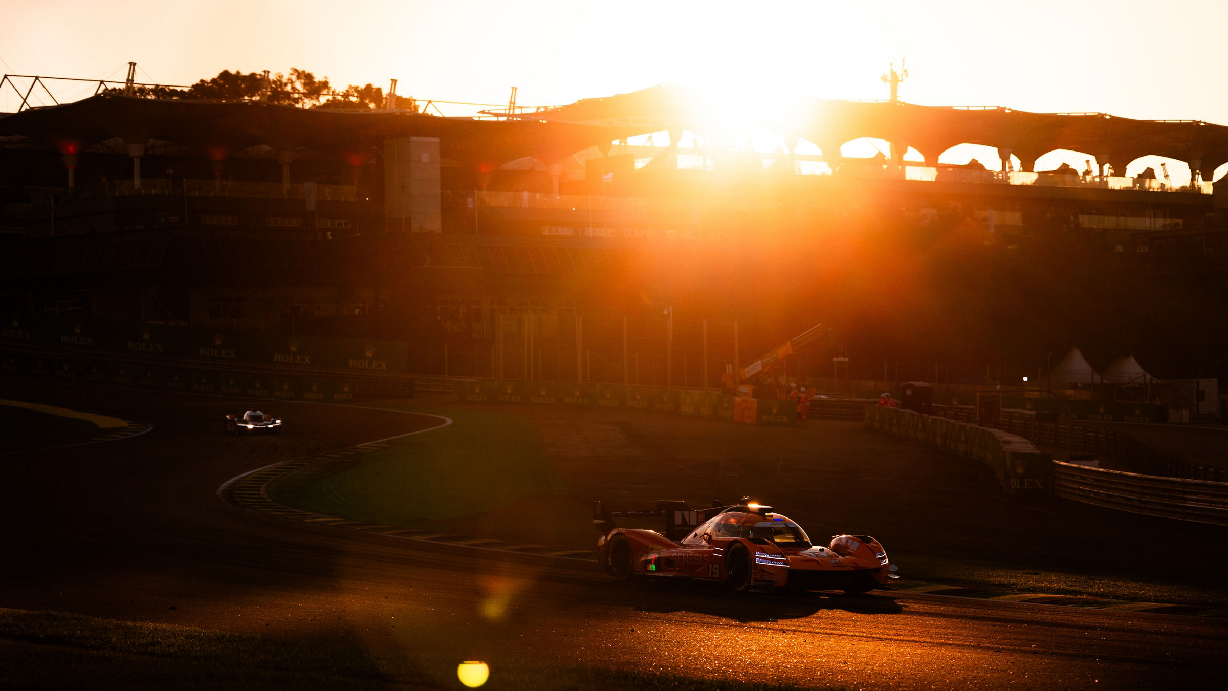 Genesis GRM-001 hypercar rounds a corner at Interlagos during sunset, with golden sunlight flooding the circuit and creating dramatic reflections across the track surface.