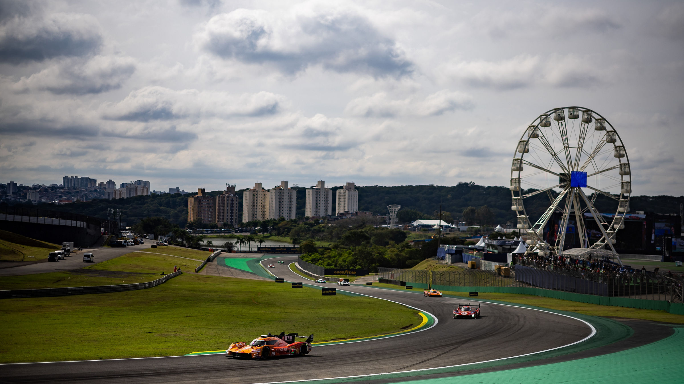 Genesis GRM-001 hypercar navigates a sweeping corner at Interlagos during the WEC São Paulo race weekend, with multiple race cars, a Ferris wheel, and the city skyline visible in the background.