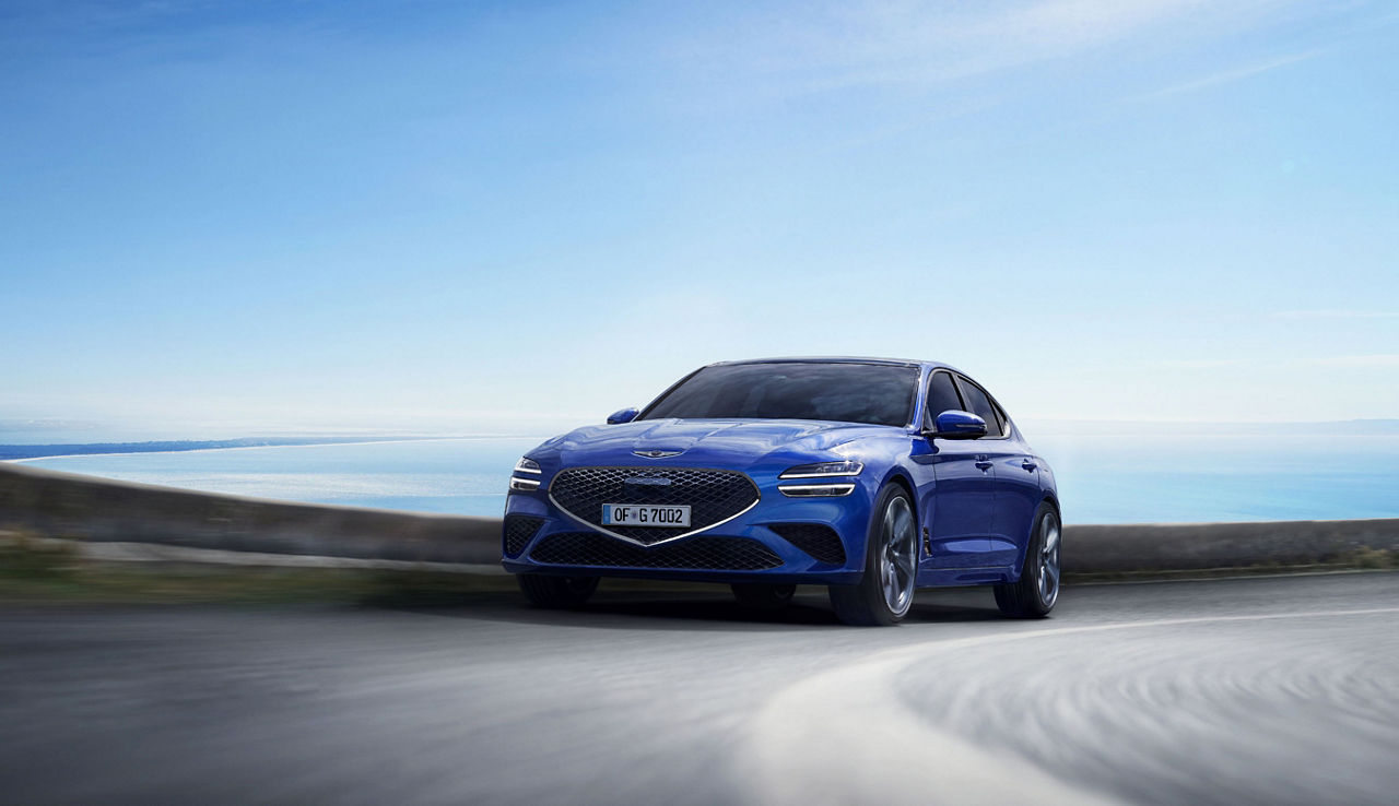 Blue Genesis G70 on a road with the sea in the background