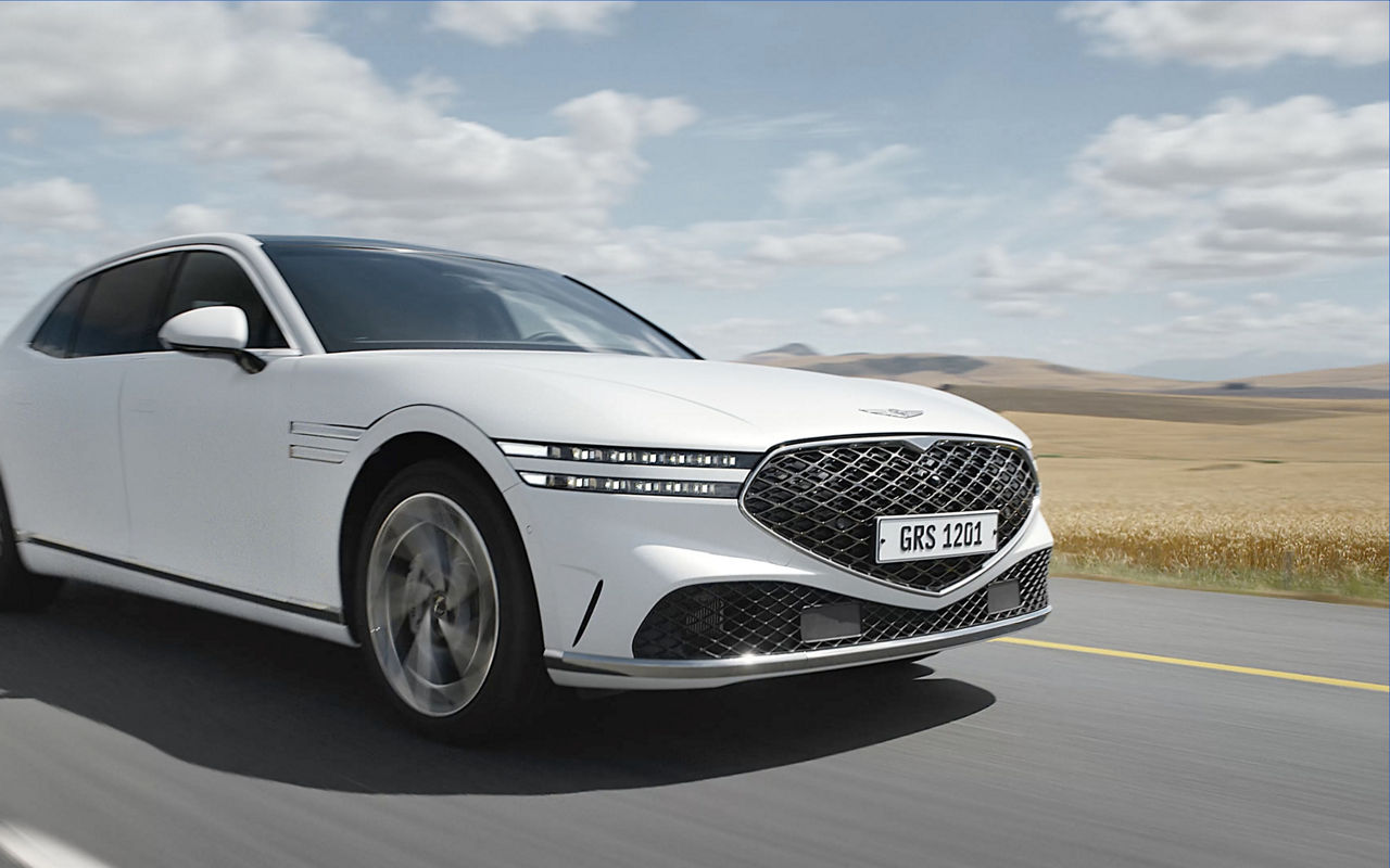 White Genesis G90 driving on a country road during the day - front side view