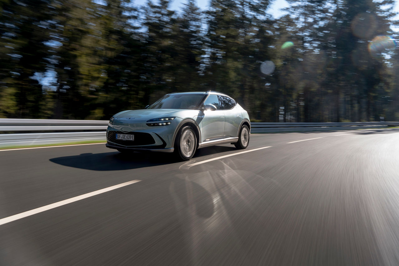 Genesis GV60 on a road with trees in the background