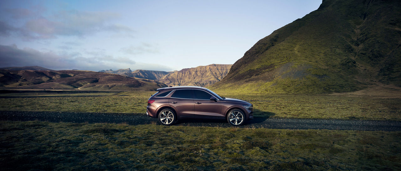 Genesis GV70 Burgundy vue de côté sur une route avant quelques montagnes