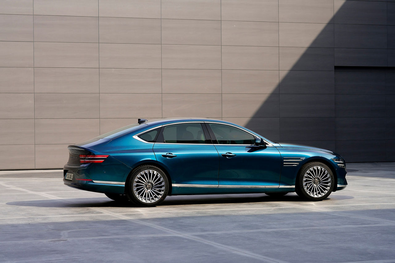 Blue Genesis G80 from the side in front of a brown wall