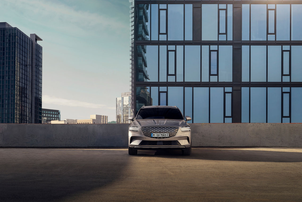 Grey Genesis GV70 from the front on a multi-storey car park with high-rise buildings in the background