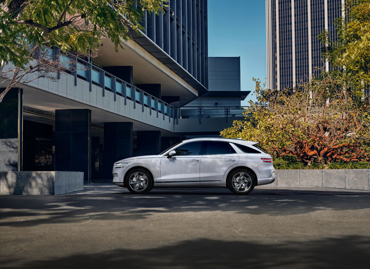 White Genesis GV70 from the side in front of a large building