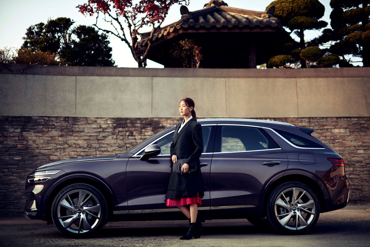 Asian woman next to the Genesis GV70 in black from the side