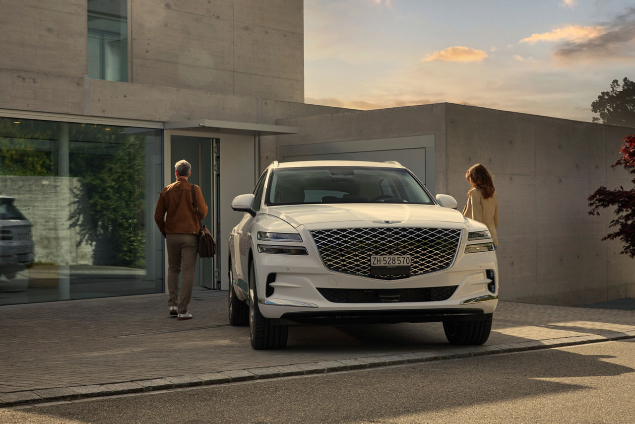 White Genesis GV80 in front of a house with two people next to it