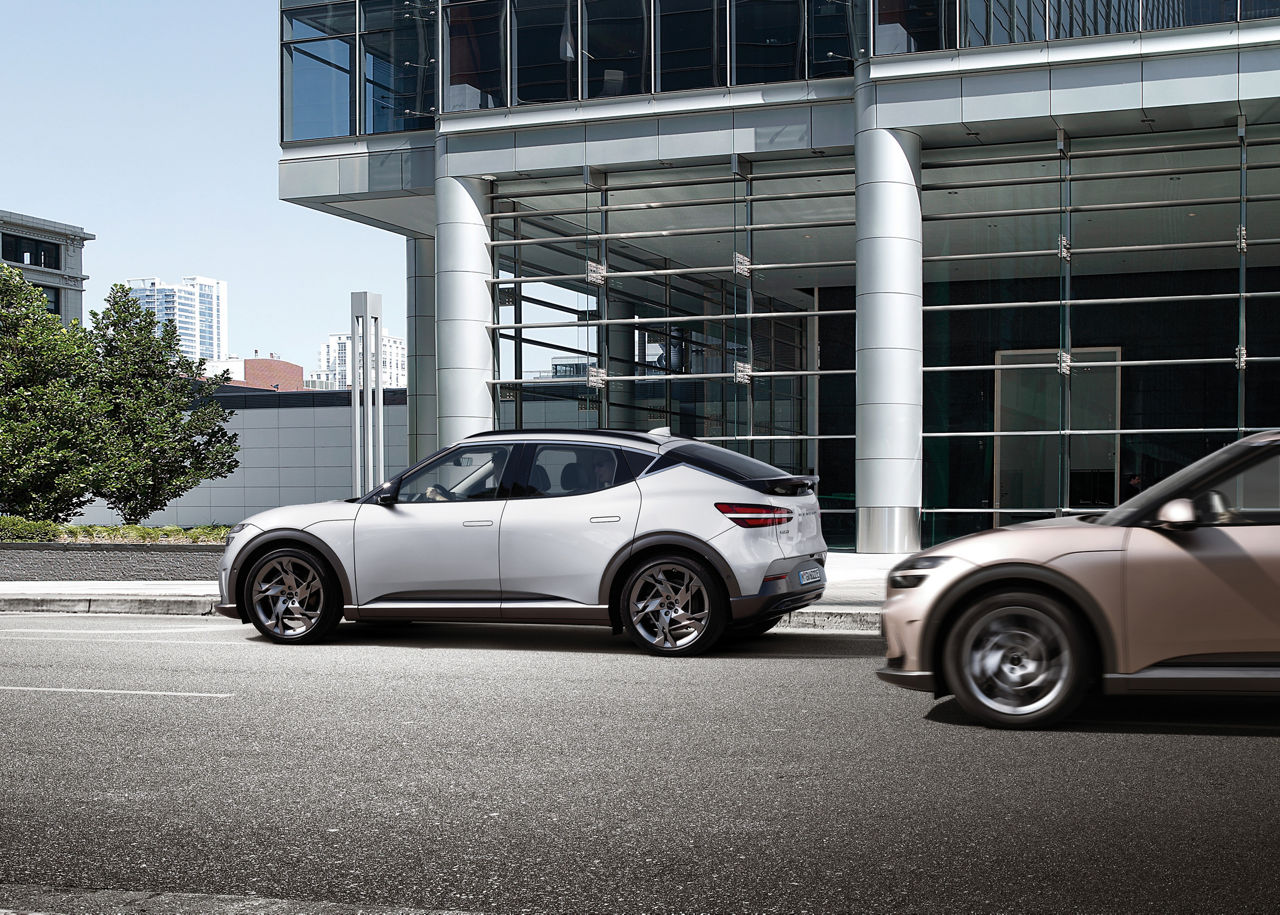 Two Genesis GV60s on a road in front of a building