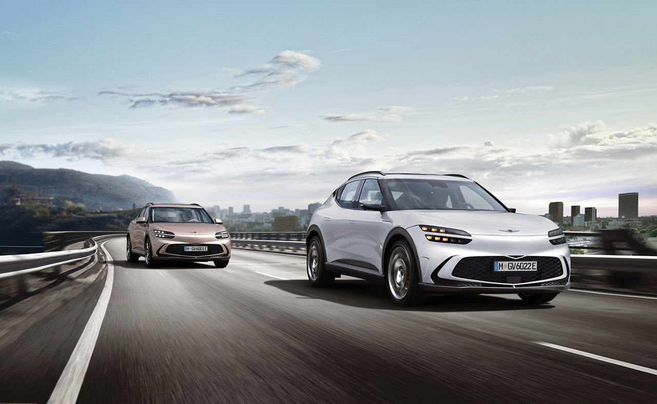 Two Genesis GV60s on a road with a city skyline in the background